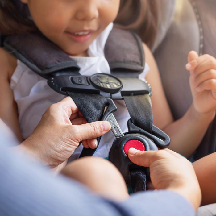Parent buckling her child's seat belt in the car. Transportation safety.