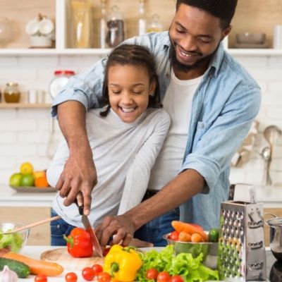 Father and daughter smiling while chopping fresh vegetables together to support immune health
