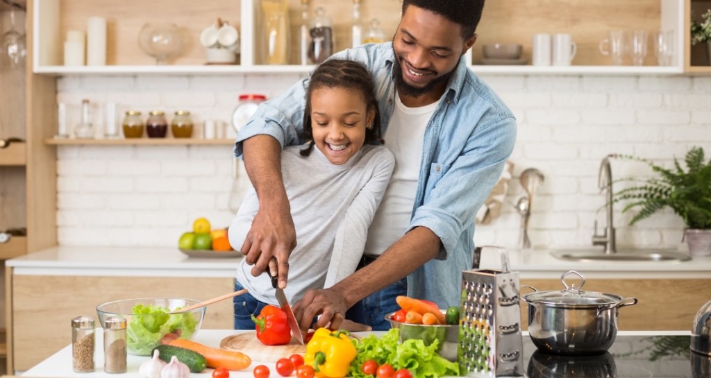 Father and daughter smiling while chopping fresh vegetables together to support immune health